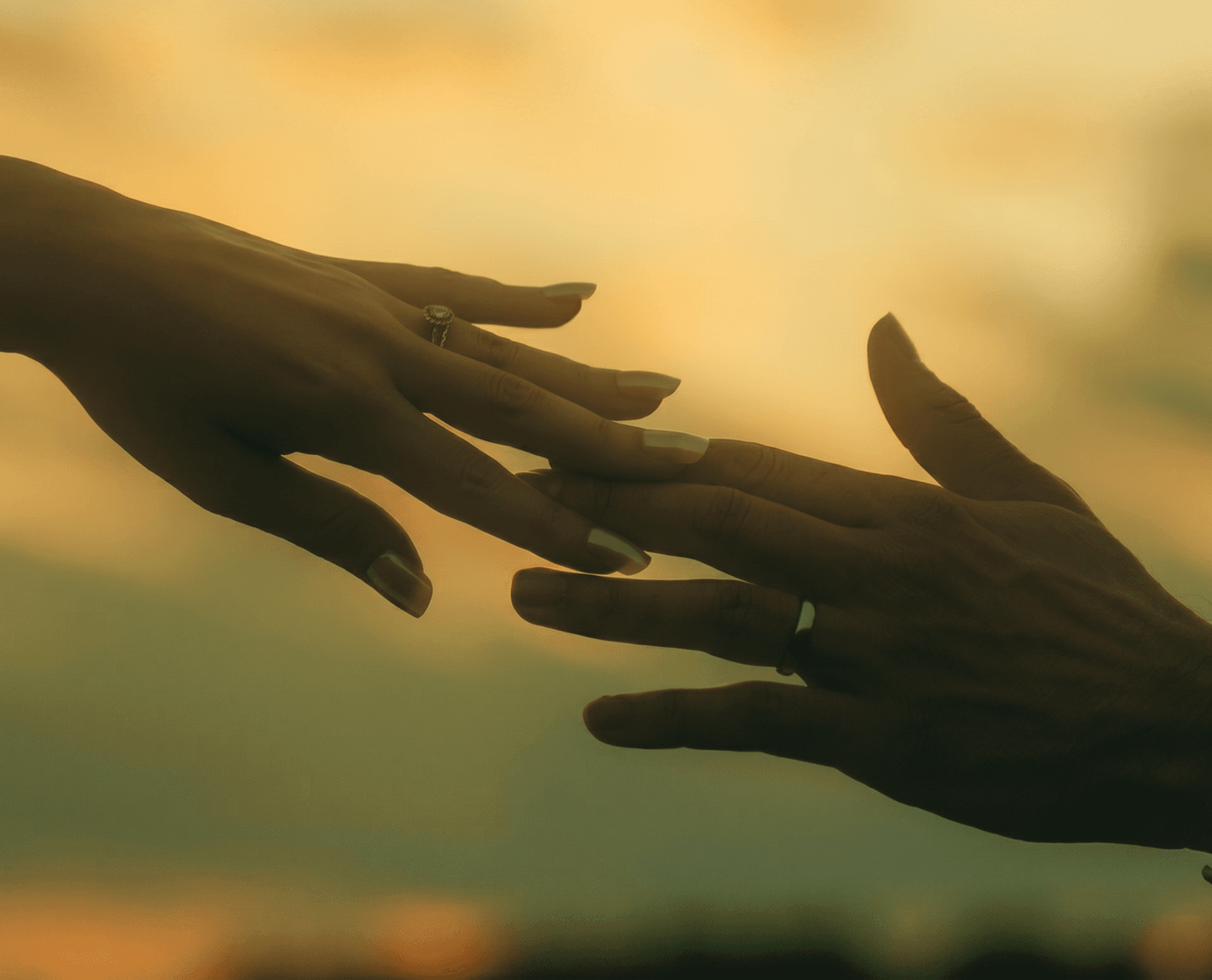 Two hands reaching toward each other at sunset
